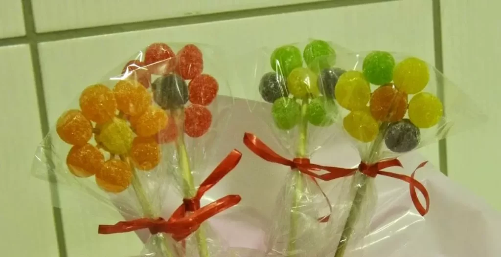 "Flores coloridas feitas inteiramente de balas de goma (jujubas), montadas em palitos e embaladas em saquinhos transparentes com laços coloridos."