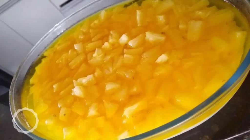 "Sobremesa gelada de abacaxi em camadas: creme amarelo na base, pedaços de abacaxi no meio e gelatina brilhante no topo, servida em um refratário transparente."