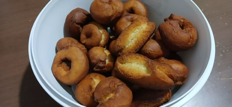 "Uma tigela cheia de rosquinhas fritas douradinhas, polvilhadas com açúcar e canela, ao lado de uma caneca de café fumegante em uma mesa de madeira."